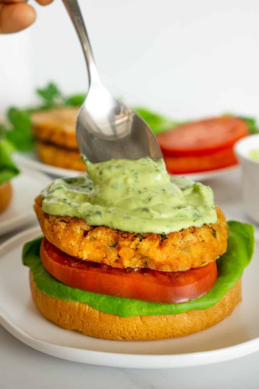 spooning avocado sauce onto lentil burgers