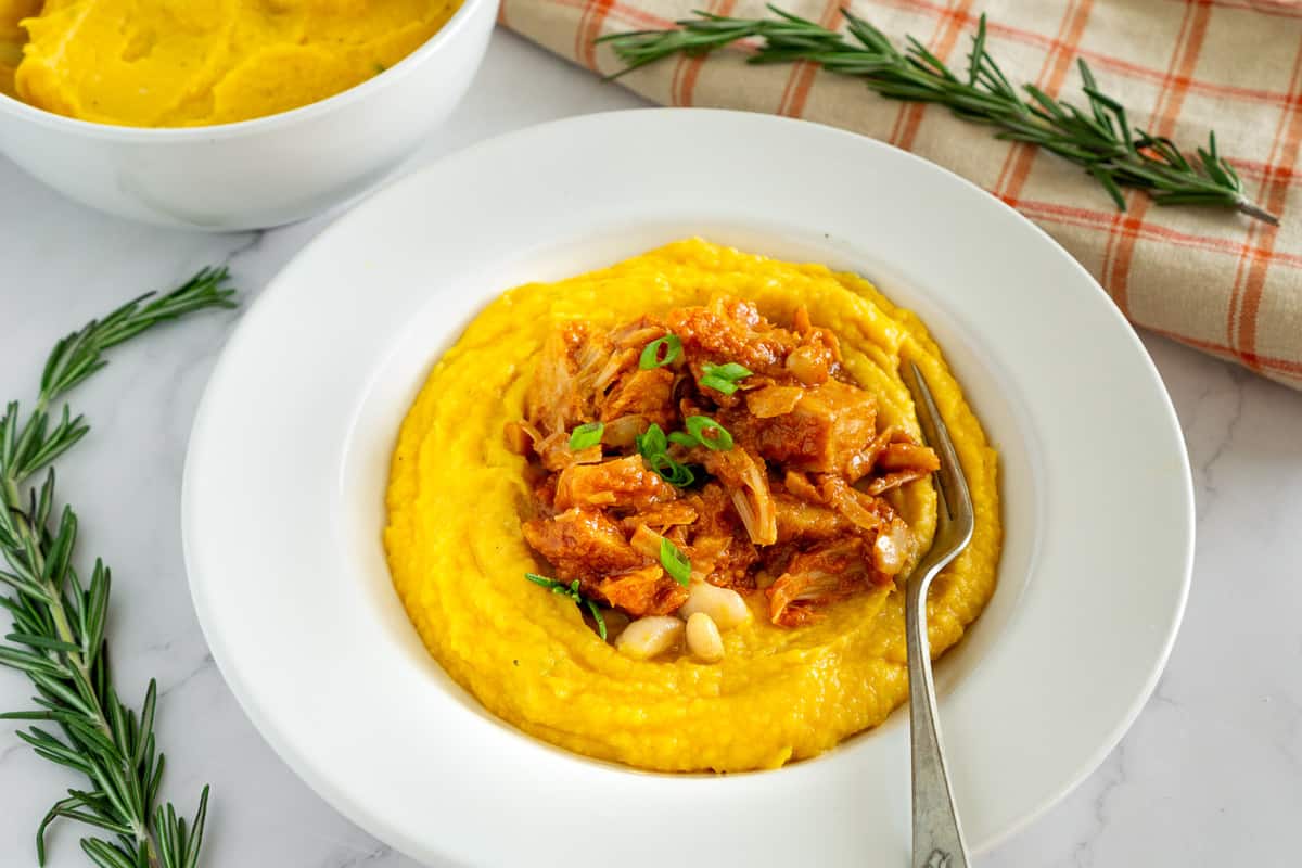 mashed butternut squash and white beans in a white plate topped with vegan bbq jackfruit