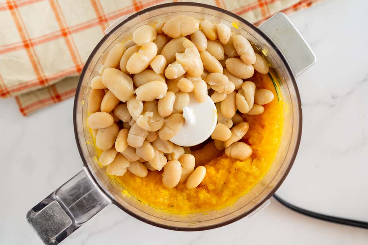 white beans on top of mashed butternut squash in a food processor