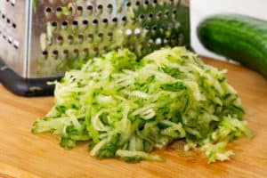 grated cucumber on a cutting board with a box grater behind it