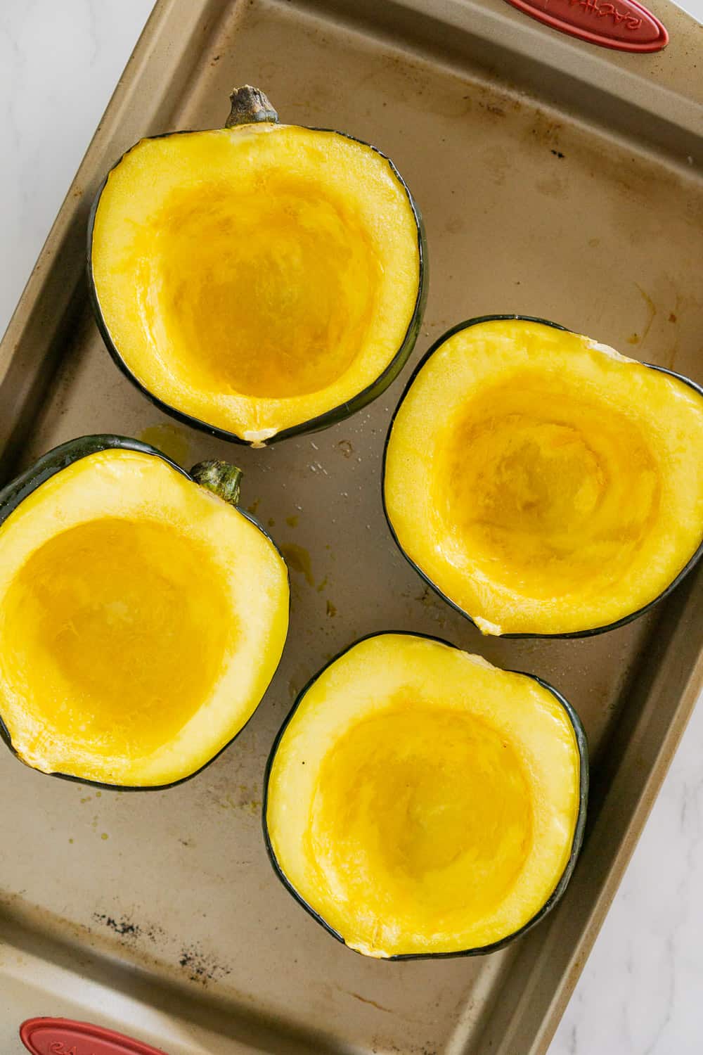 overhead image of halved roasted acorn squash in a roasting pan