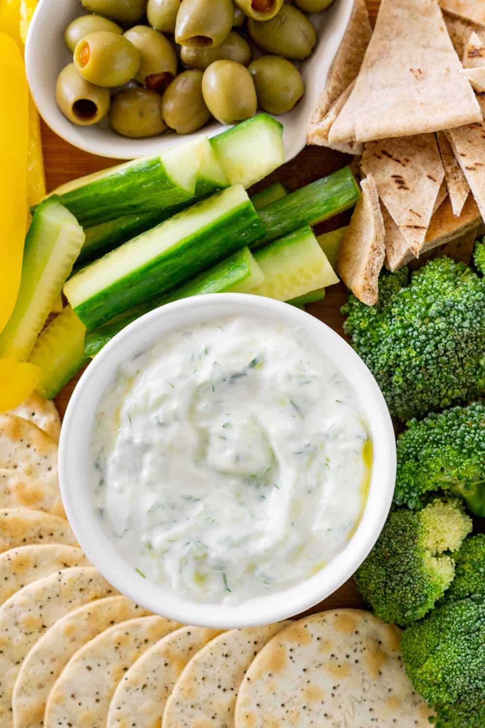 bowl of dairy free tzatziki on a vegan charcuterie board with broccoli, crackers, cucumbers, etc for dipping