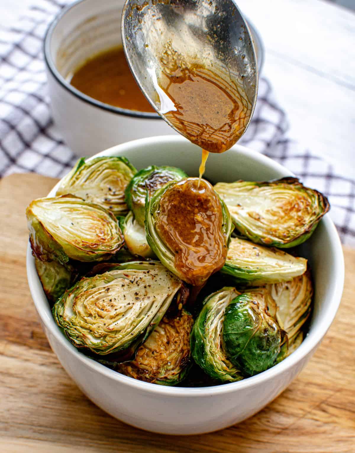 bowl of vegan roasted brussels sprouts with balsamic maple dressing being drizzled on top