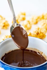 bowl of melted dark chocolate with a spoon, with popcorn balls in the background