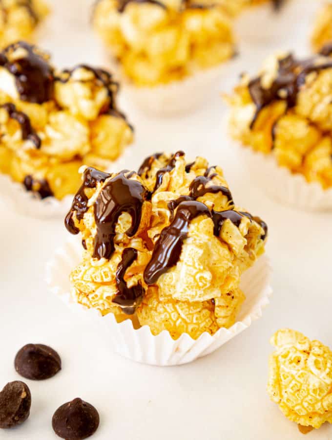 close up of chocolate popcorn ball in a muffin liner with chocolate chips on the side