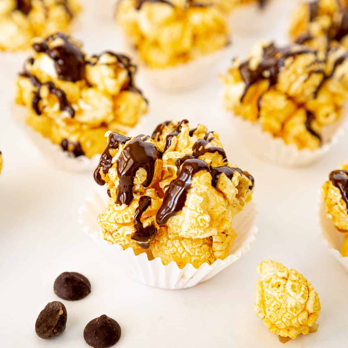 close up of chocolate popcorn ball in a muffin liner with chocolate chips on the side
