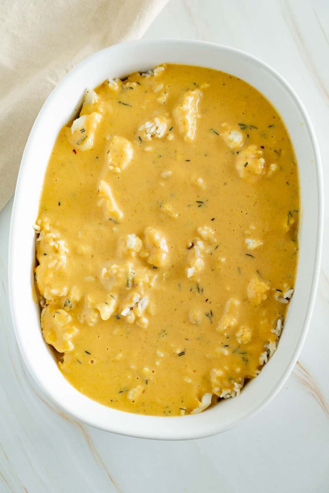 vegan cheesy sauce poured over cauliflower and rice in a casserole pan