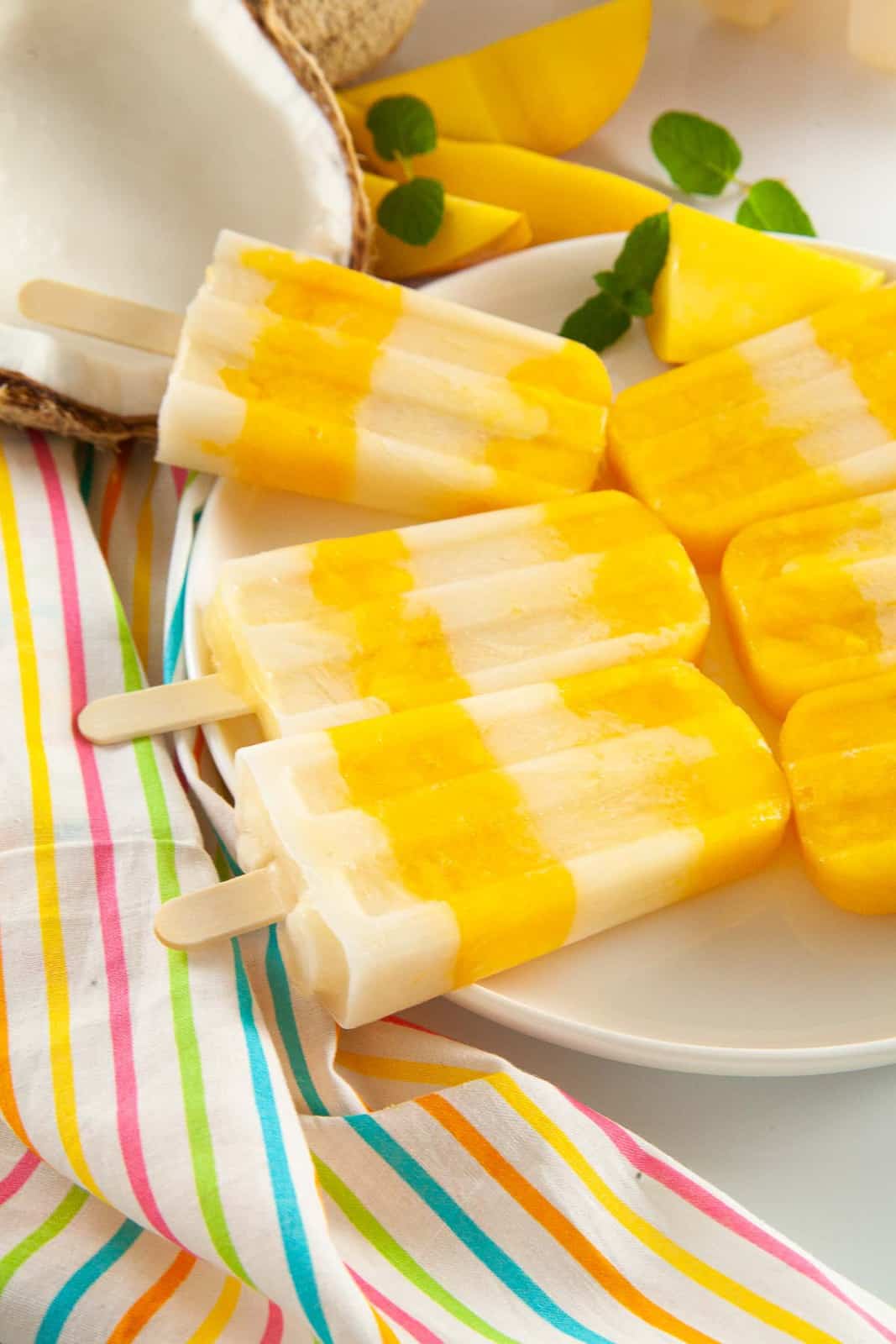 Layered mango popsicles with coconut milk on a plate.