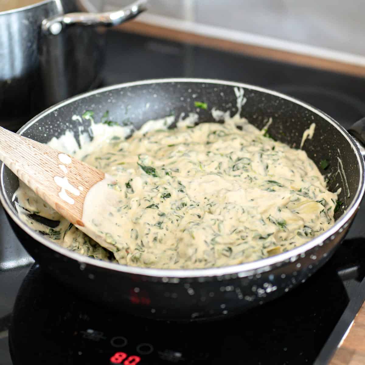 Vegan creamy spinach artichoke Alfredo sauce in a pan.