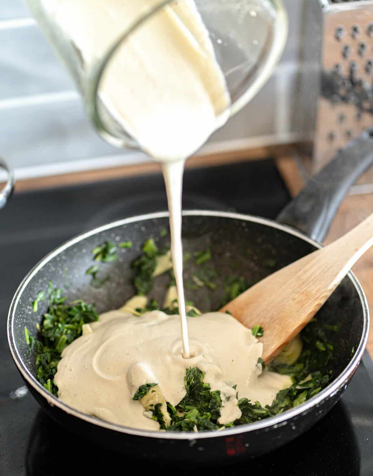 Pouring vegan creamy cashew sauce over spinach and artichoke.