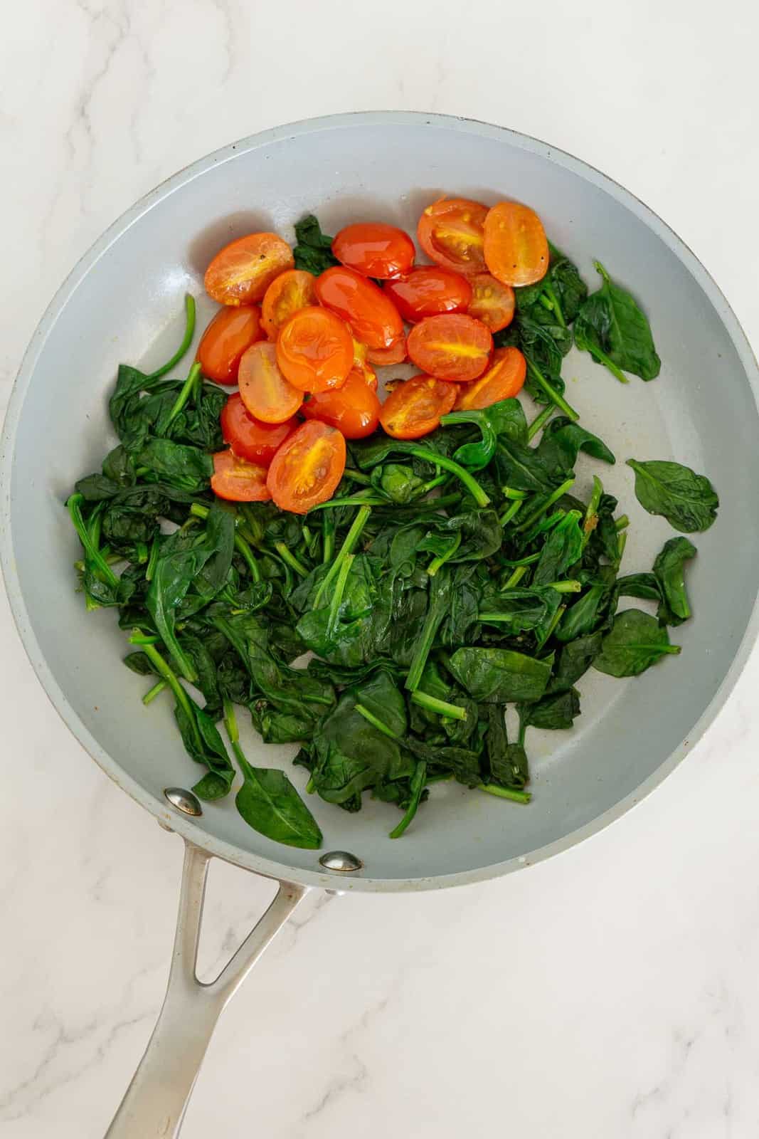 Sauteed spinach and tomatoes in a skillet.