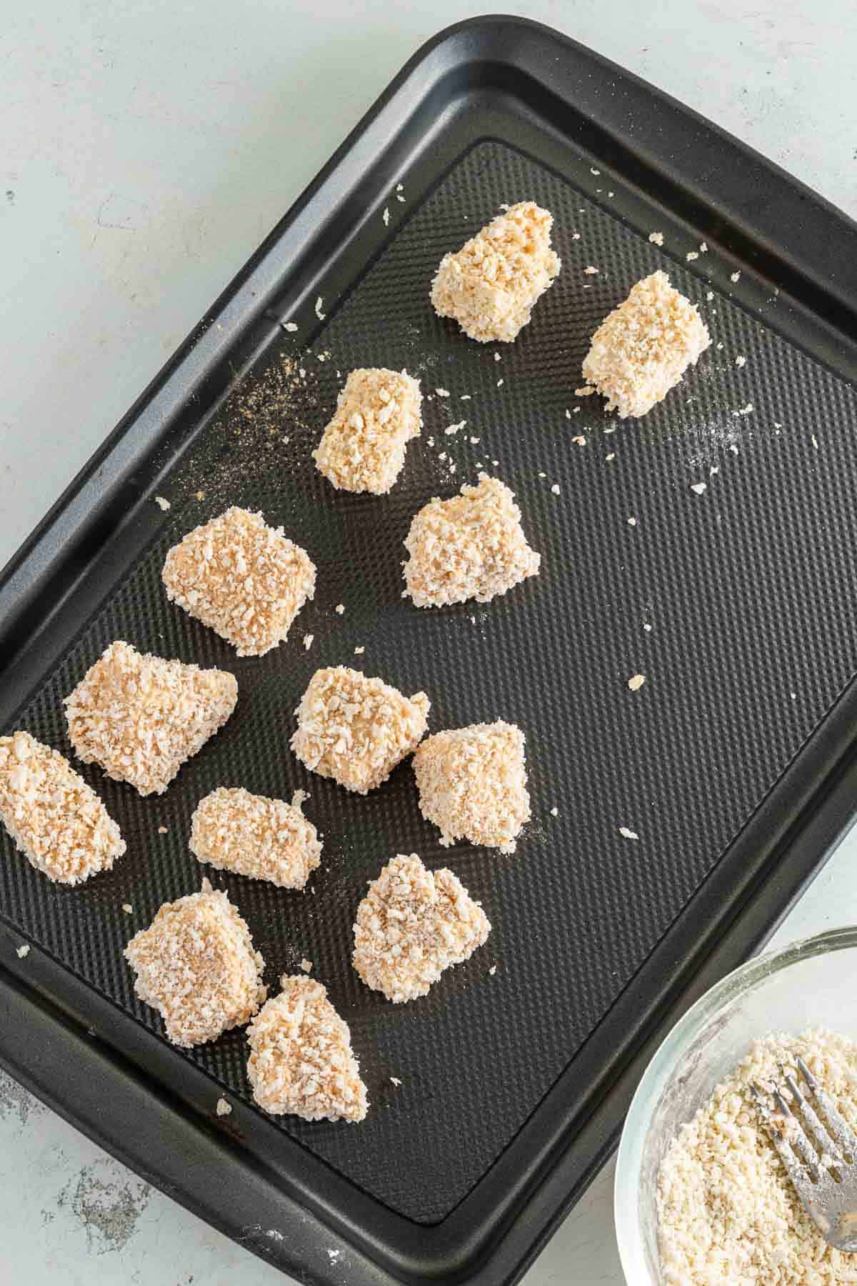 Tofu nuggets dipped in panko breadcrumbs on a baking pan.