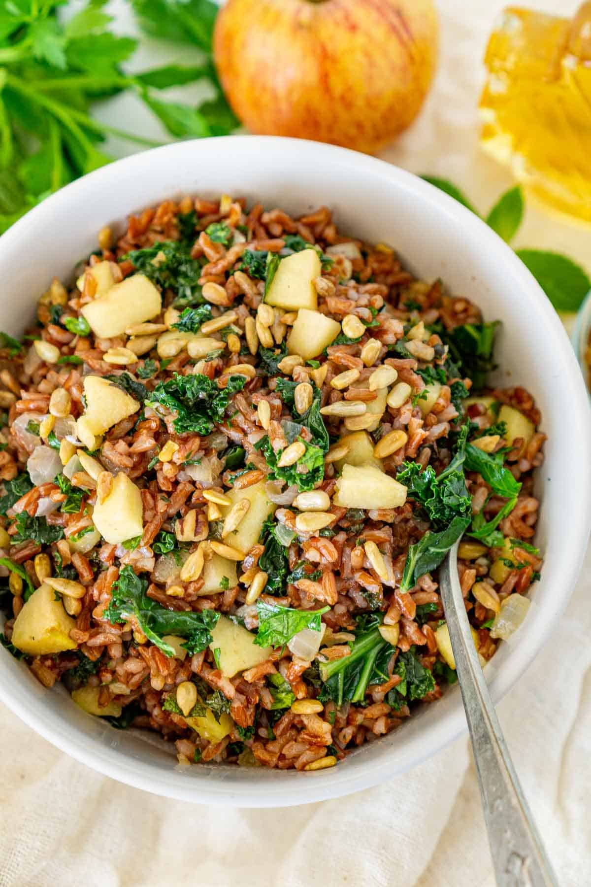 Vegan rice salad with kale and apples in a white bowl.