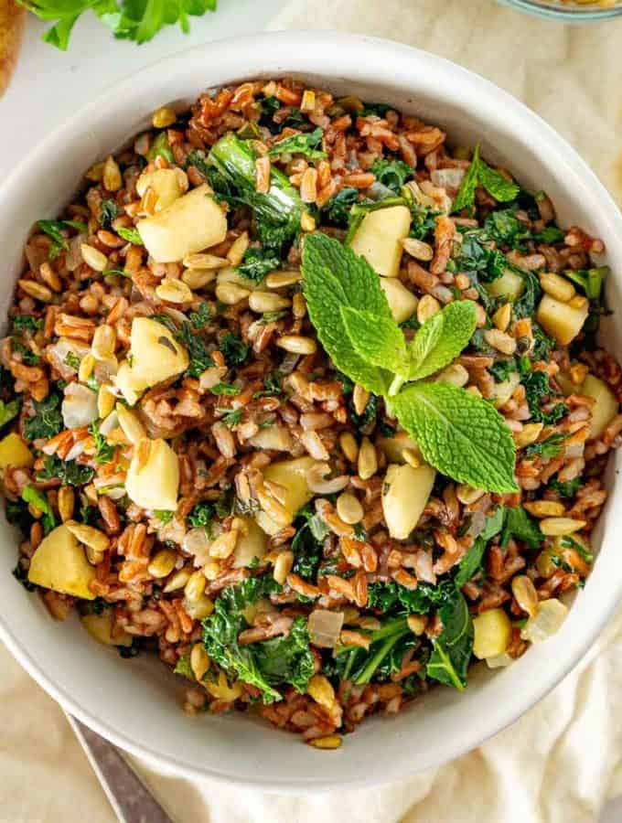 Red rice salad with apples and kale in a white bowl.