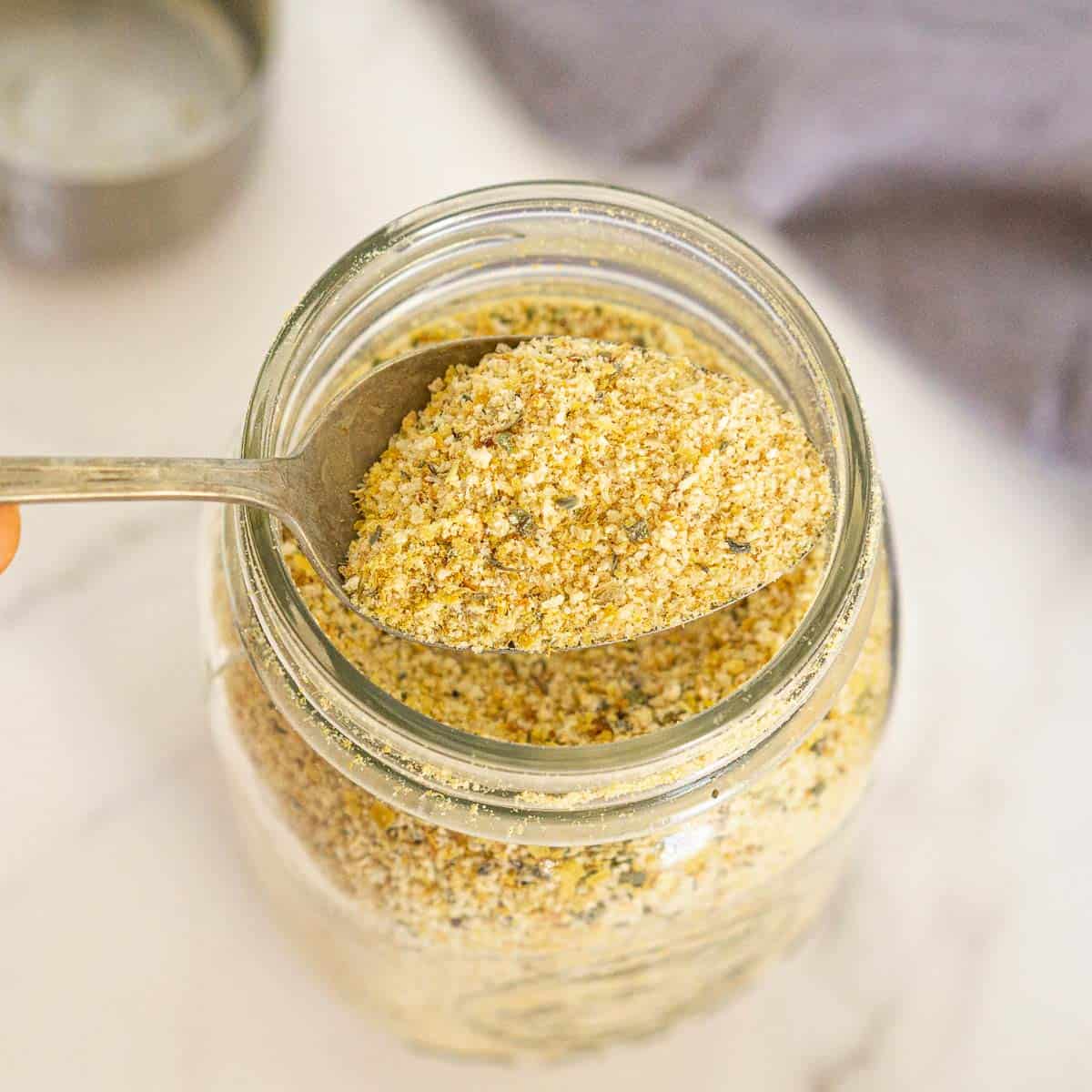 Scooping out vegan seasoned bread crumbs with a spoon.