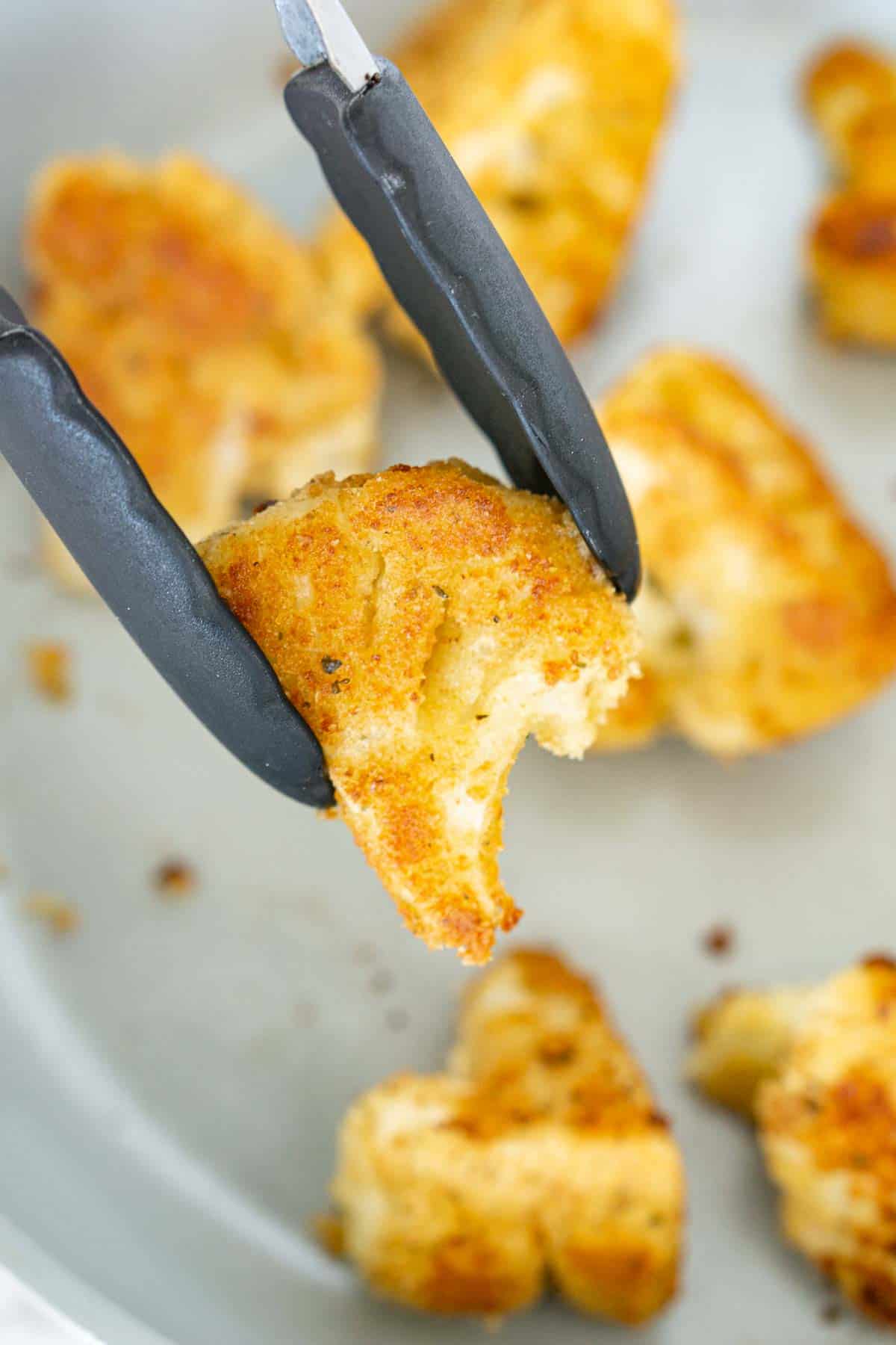 Tongs holding piece of crispy fried vegan cauliflower.