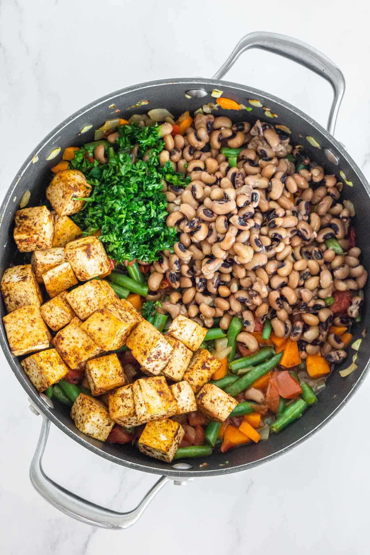 Black eyed peas, blackened tofu, and herbs added to a casserole pan with veggies.