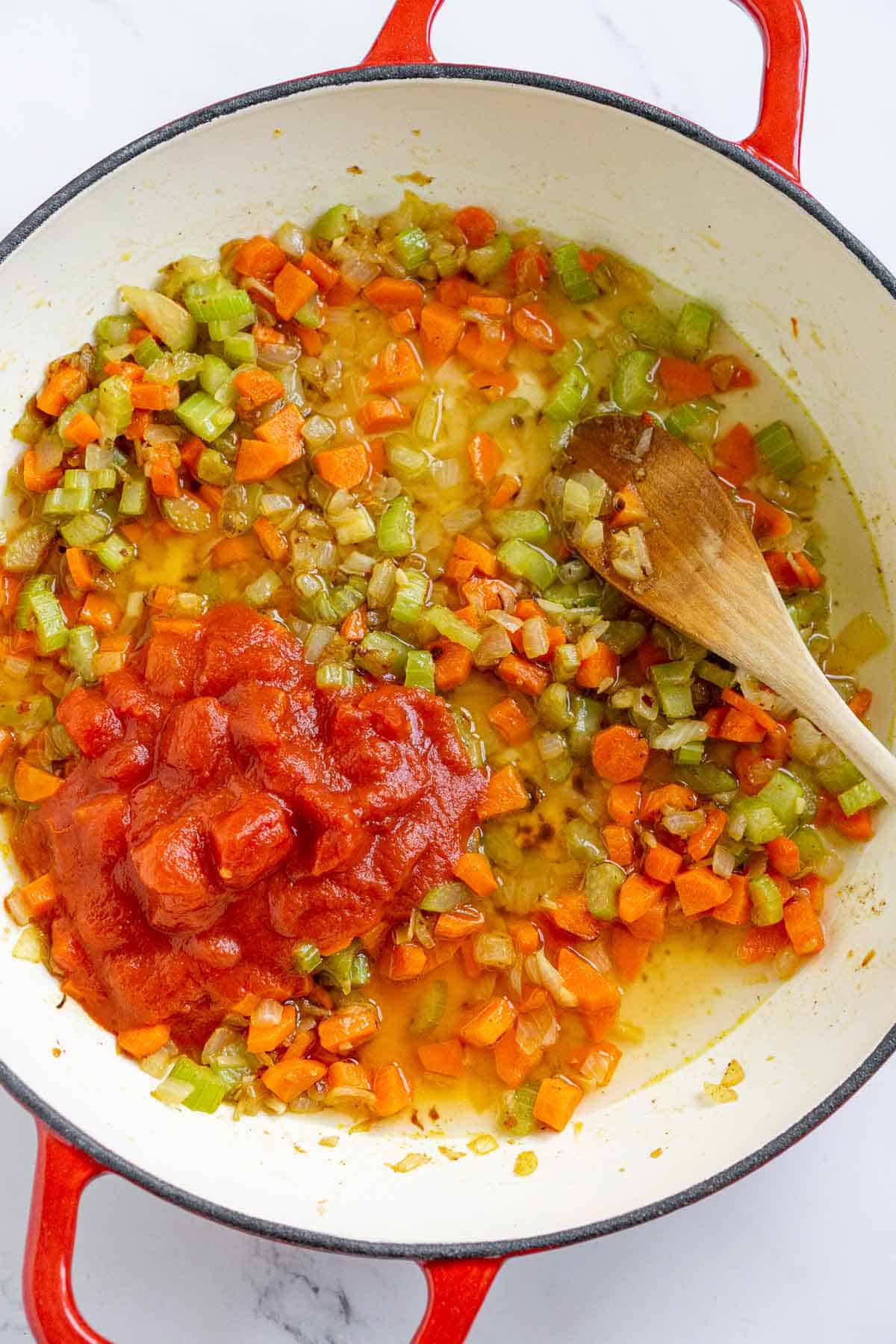 Adding broth and diced tomatoes to sautéed veggies.