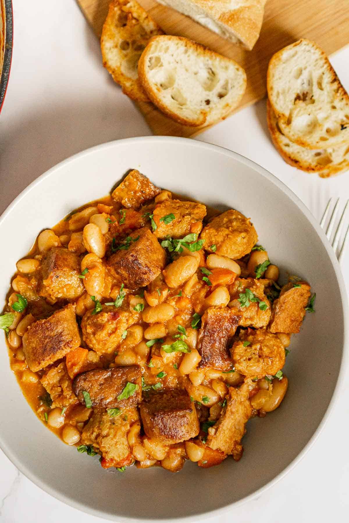 Bowl of vegan sausage stew with toasted baguette.