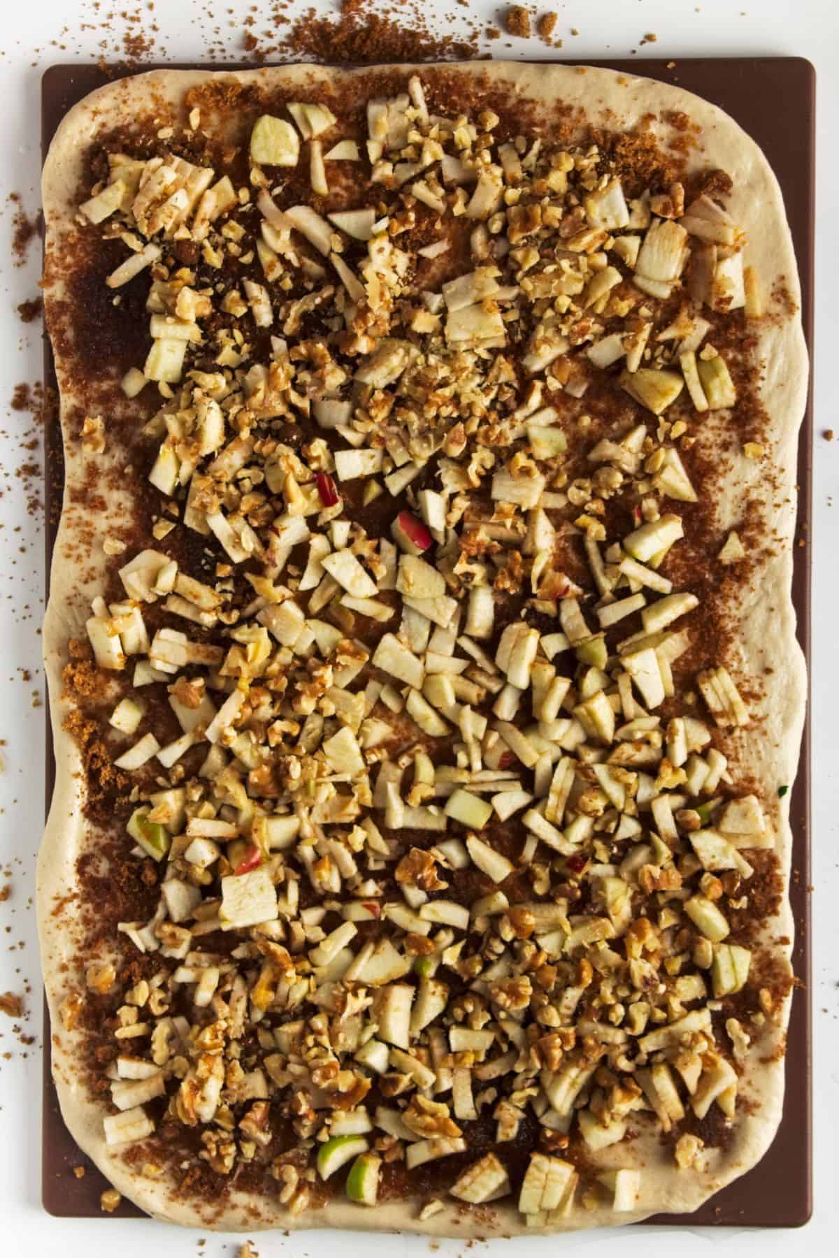 Sticky bun dough rolled out with nuts and apples spread on top