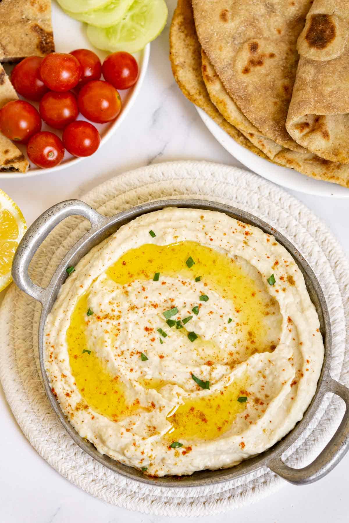 Butterbean hummus in a bowl with pita, tomatoes, cucumbers on the side