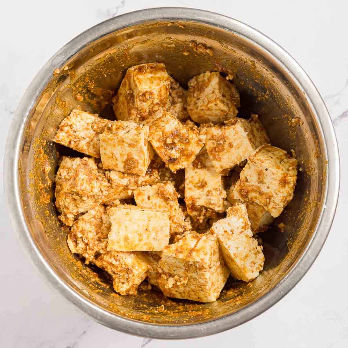 Bowl of tofu pieces marinating in shawarma seasoning
