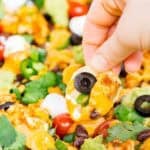 Hand holding vegan nachos loaded with tofu crumbles, vegan queso, and other vegan toppings
