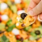 Hand holding vegan nacho loaded with vegan queso and other toppings